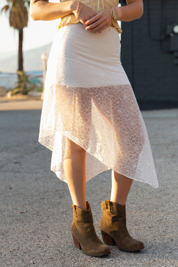 Person wearing a white lace skirt and brown boots on a street.