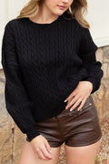 A woman wearing a black cable-knit crewneck sweater and brown faux-leather pants, shown from the side against a neutral outdoor background.