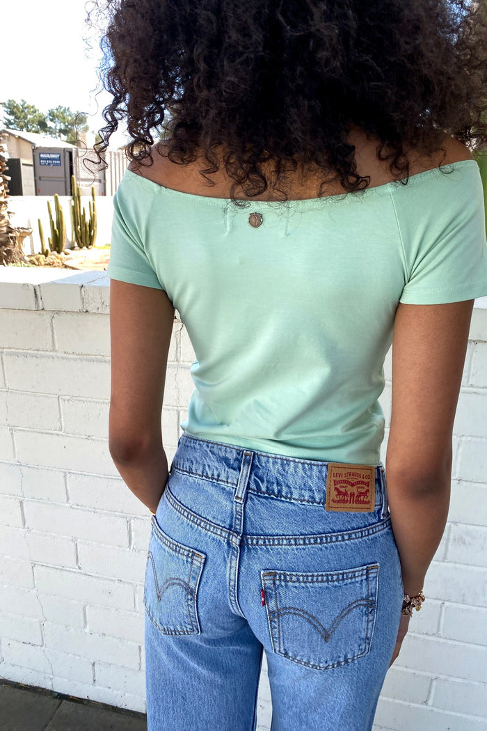 Person wearing a light green off-shoulder top and blue jeans with Levi's branding.