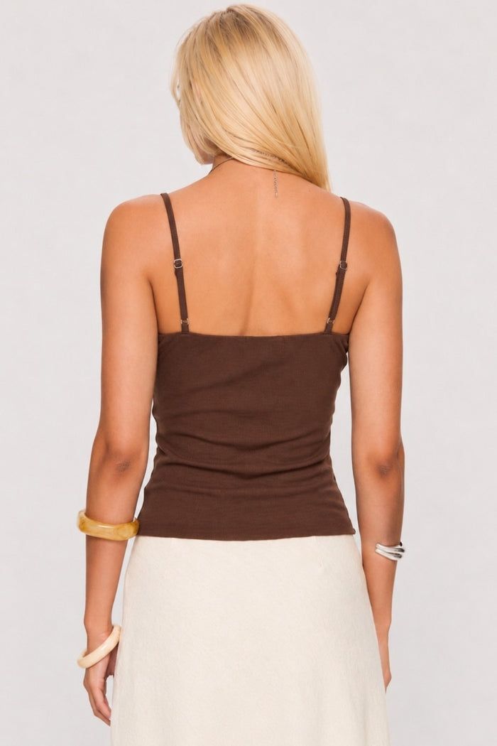 Woman wearing a brown tank top and white pants against a plain background