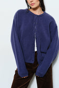 A woman wearing a navy blue knit cardigan with a crew neck and button front, paired with brown pants, against a plain light background.