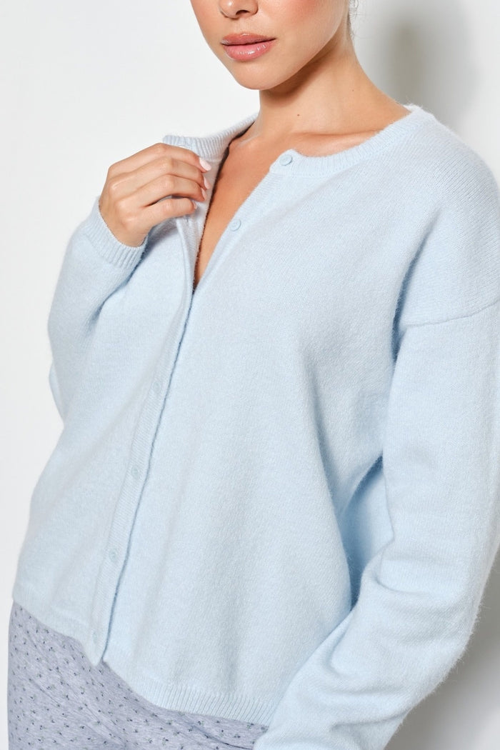 A woman wearing a light blue knit cardigan sweater with a buttoned front and long sleeves, shown against a plain light background.
