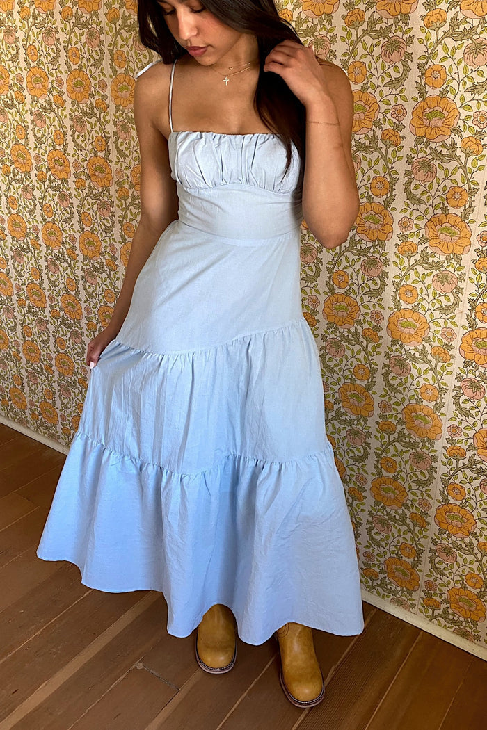 Woman wearing a light blue dress with floral wallpaper in the background