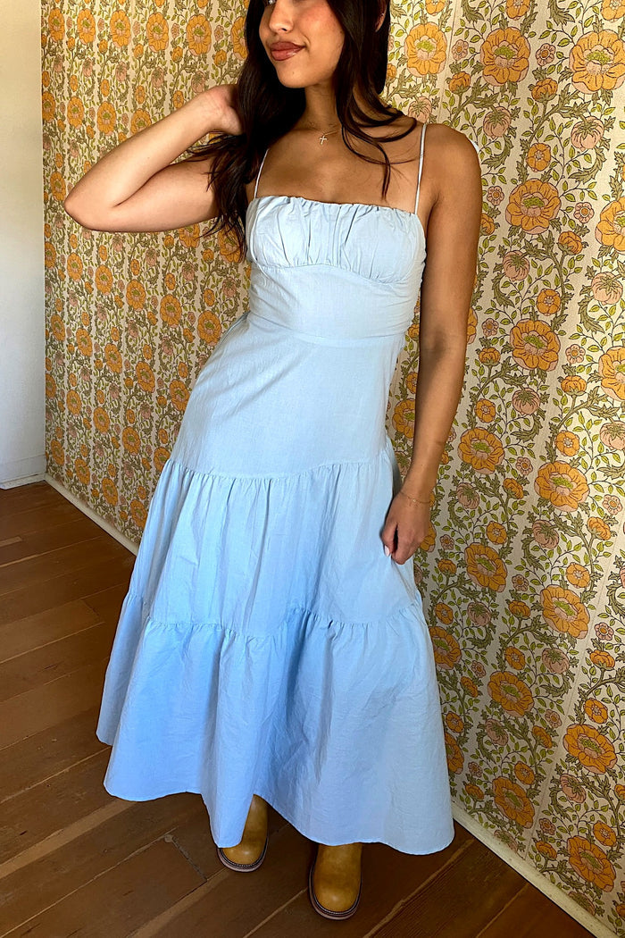Woman wearing a light blue dress standing against a floral wallpapered wall.