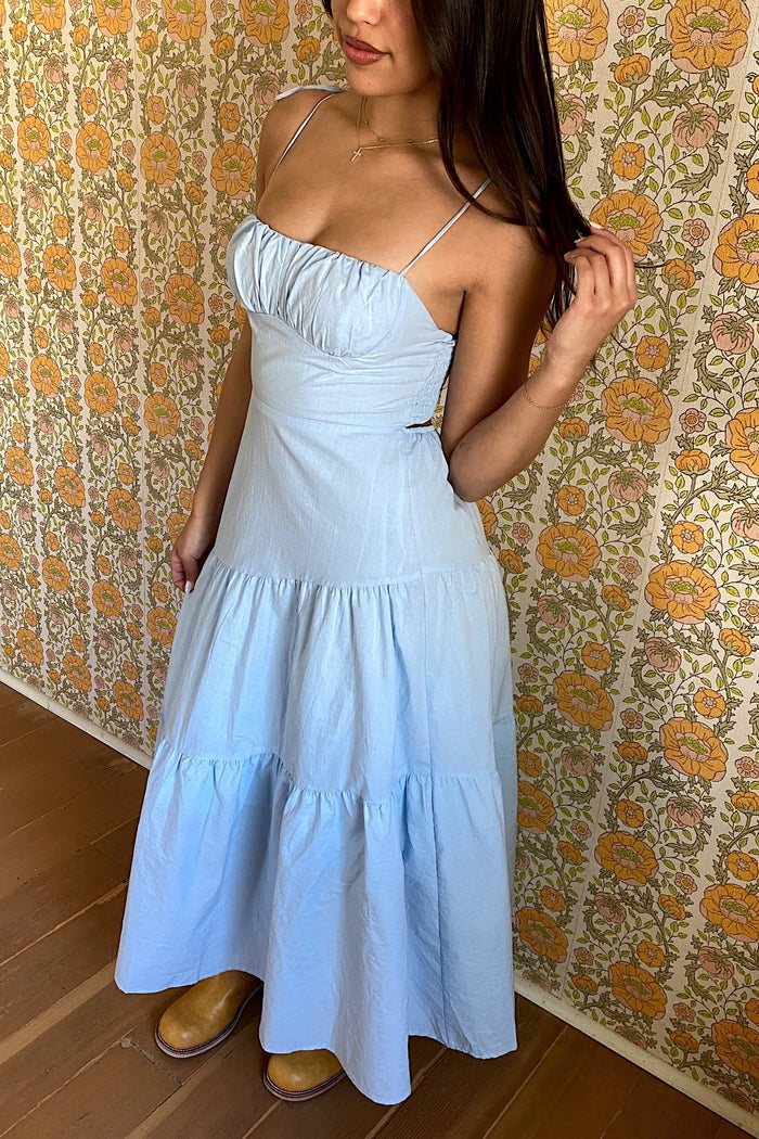 Woman wearing a light blue dress against a floral wallpapered wall.