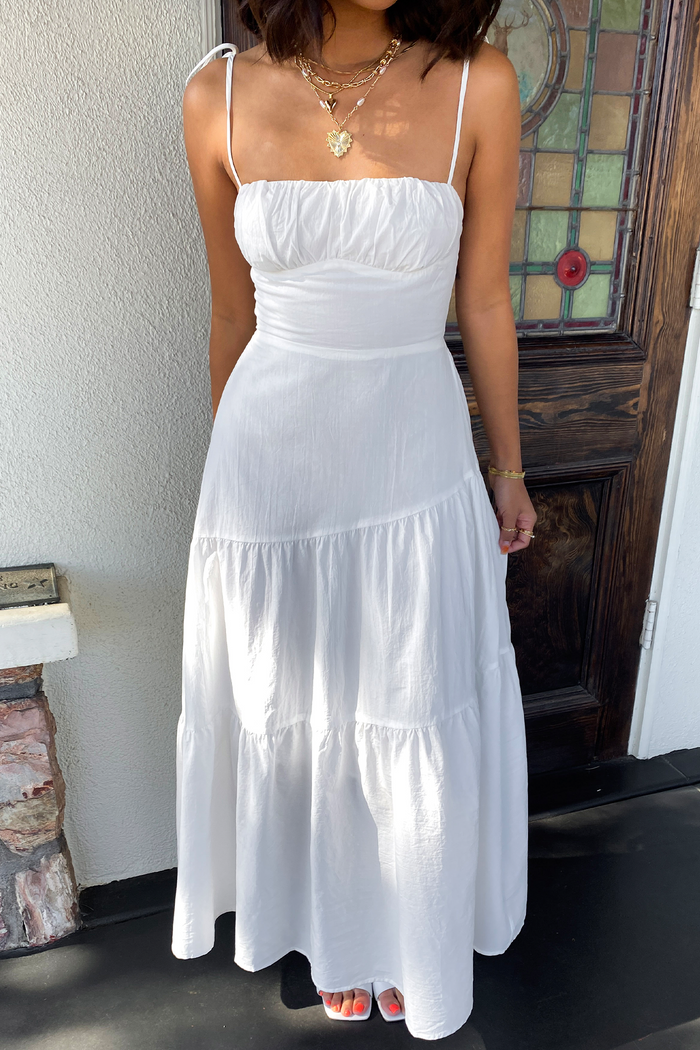 Woman wearing a white dress standing in front of a stained glass window.