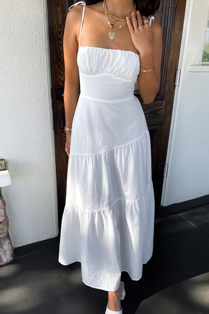 Person wearing a white dress standing indoors with a neutral background