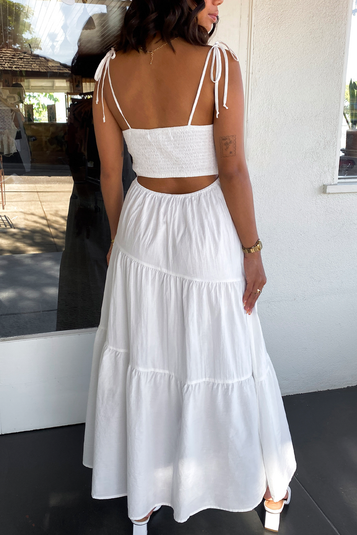 Woman wearing a white dress with thin straps in an outdoor setting.