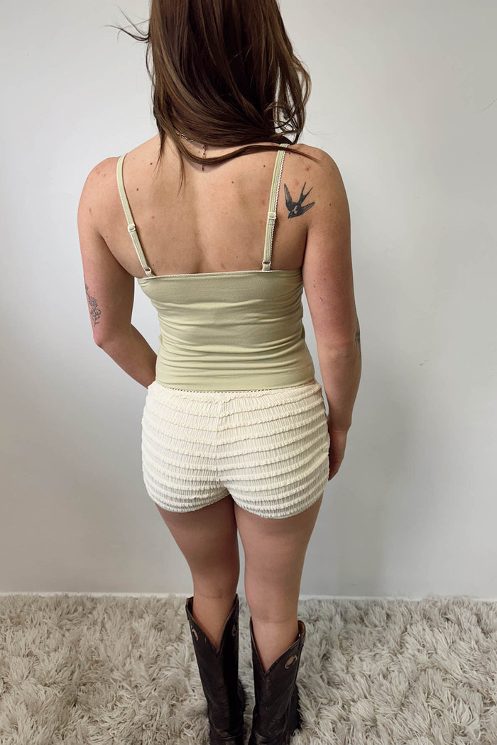 Person wearing a light green tank top and white shorts with black cowboy boots, standing against a plain background.