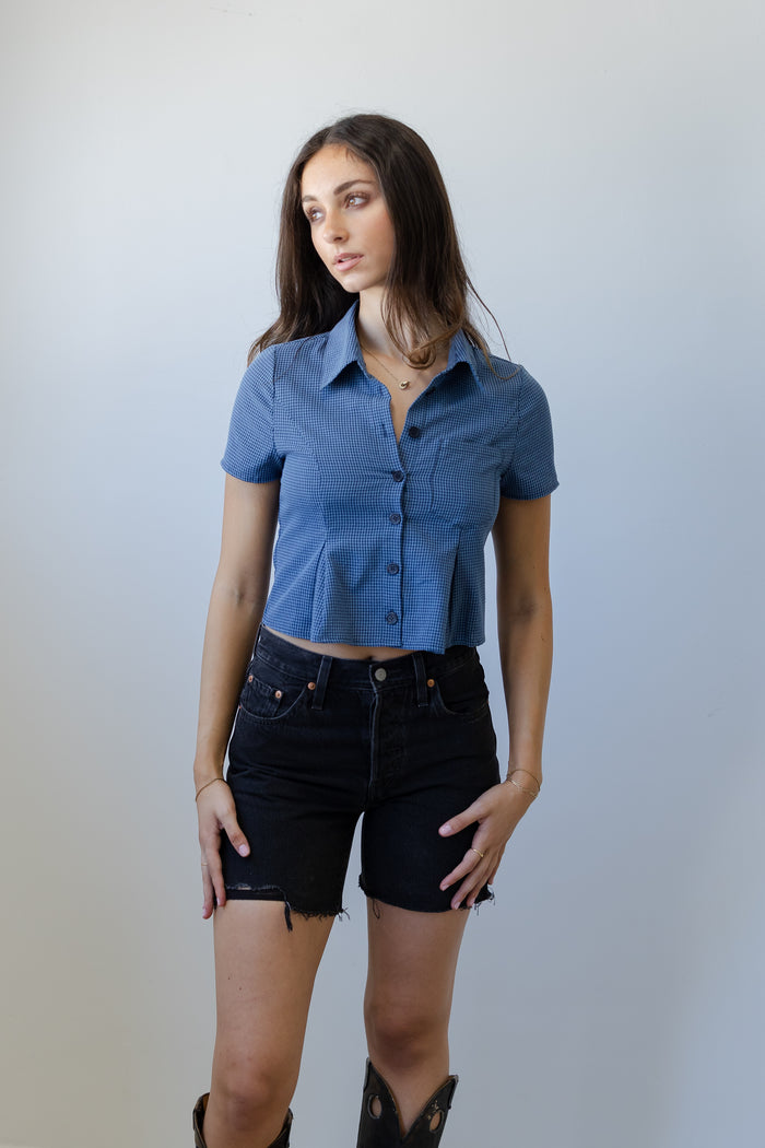 Woman wearing a blue shirt and black shorts against a plain background