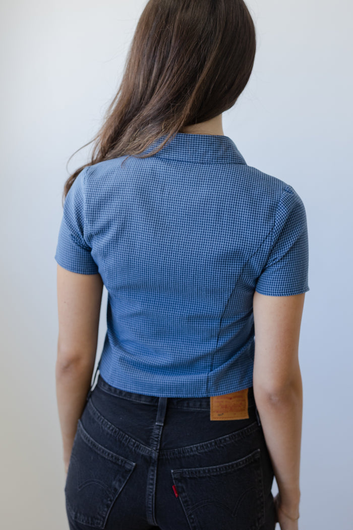 Person wearing a blue patterned shirt and dark jeans against a plain background
