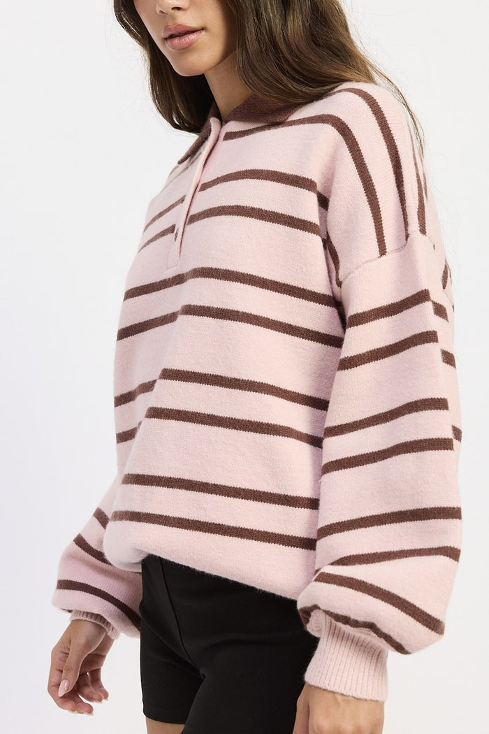 A woman wearing a fuzzy knit half-zip pullover sweater with horizontal brown stripes on a light pink background, paired with black pants.