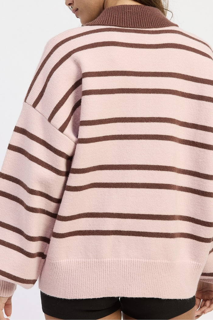 A close-up back view of a person wearing an oversized knit sweater with horizontal brown stripes on a pale pink background.