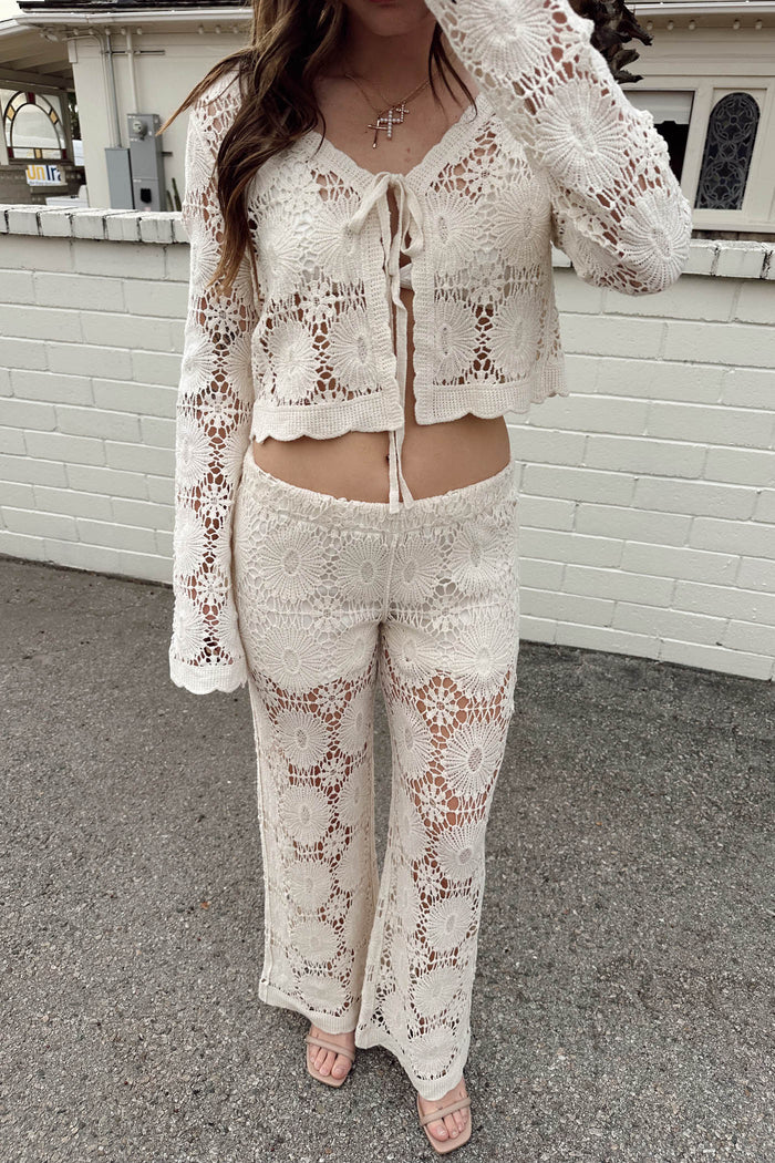 Person wearing a white lace outfit standing against a white brick wall.