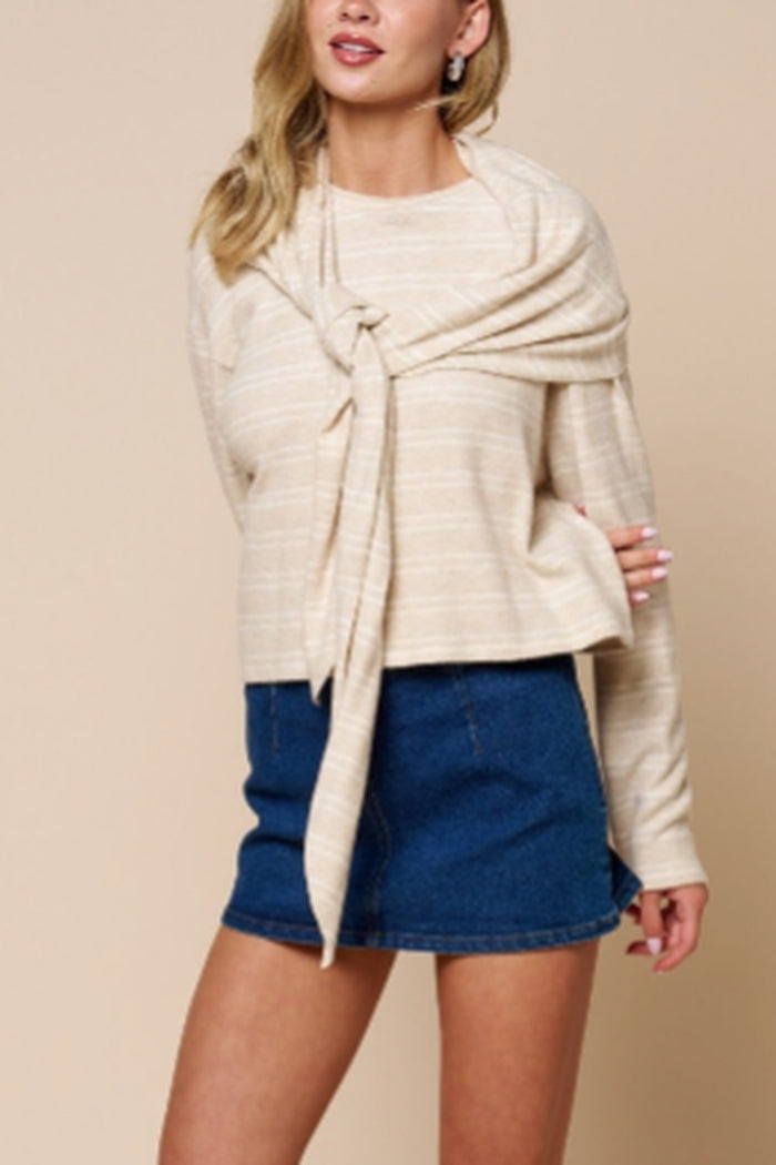 A woman wearing a cream and beige horizontally striped knit wrap sweater tied at the front, paired with a blue denim mini skirt, against a solid beige studio background.