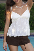 Woman wearing a white floral top and brown shorts by a pool
