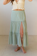 Person wearing a light green tiered skirt with a white top against a plain background