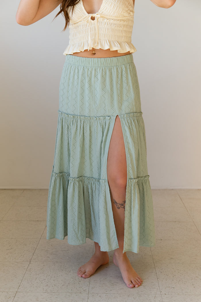 Person wearing a light green tiered skirt with a white top against a plain background