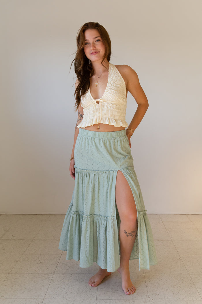 Woman wearing a light-colored top and green skirt against a plain background