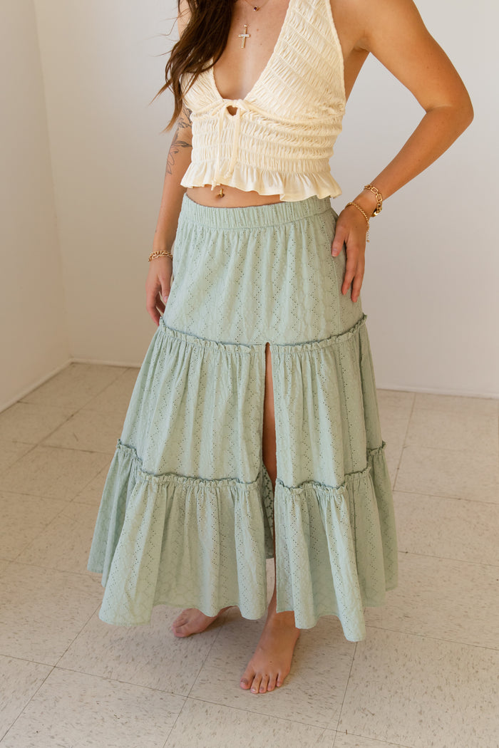 Woman wearing a light green tiered skirt and beige top against a white background