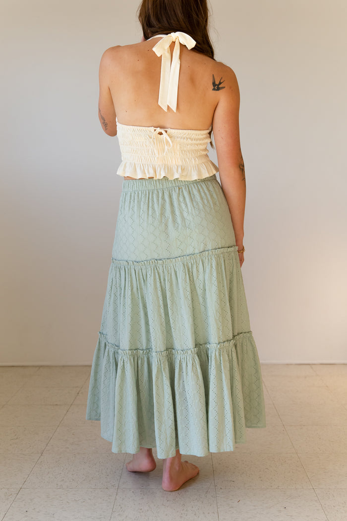 Woman wearing a light green tiered skirt and cream top against a white background
