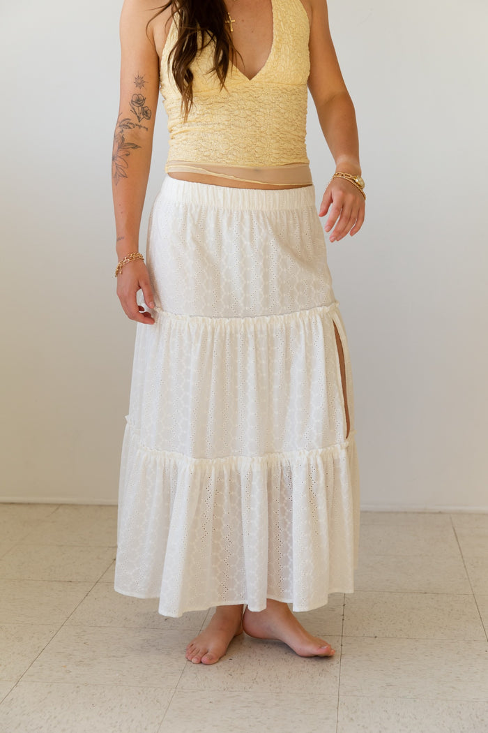 Woman wearing a yellow top and white tiered skirt against a plain background