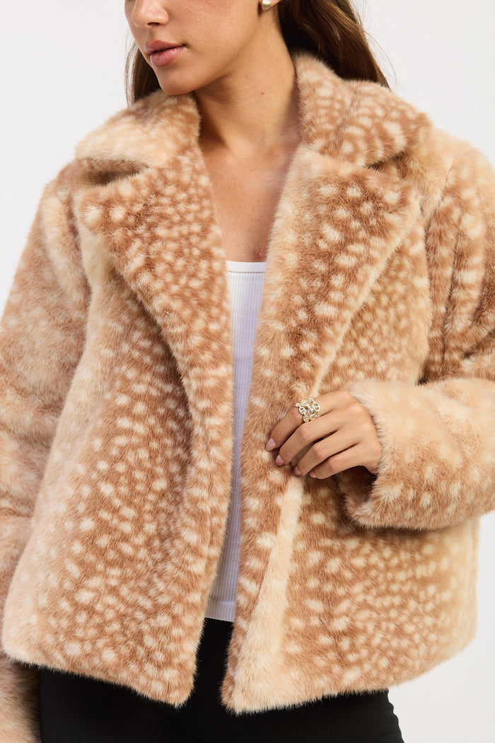 A close-up of a woman wearing a fuzzy faux-fur jacket with a light beige and white spotted pattern, styled over a white top and black pants.
