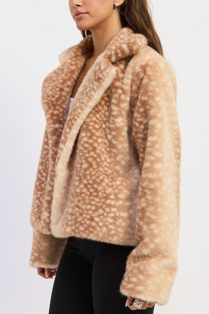 A woman wearing a fuzzy faux fur jacket in a light tan and beige spotted pattern, paired with black pants, shown against a plain white background.