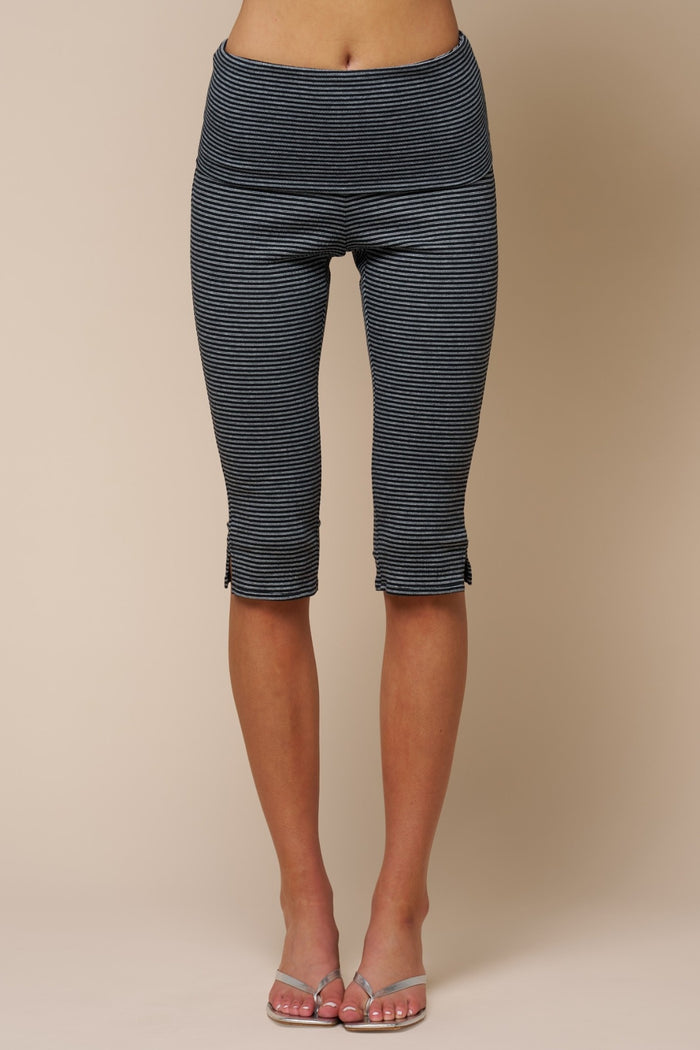 A person wearing dark gray and white striped capri leggings, shown from the waist down against a plain beige studio background.