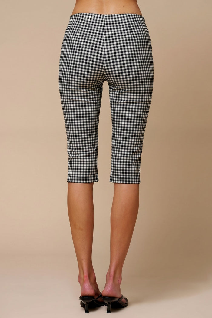 Black and white gingham capri pants shown from the back on a model, paired with black pointed-toe mule heels against a solid beige studio background.