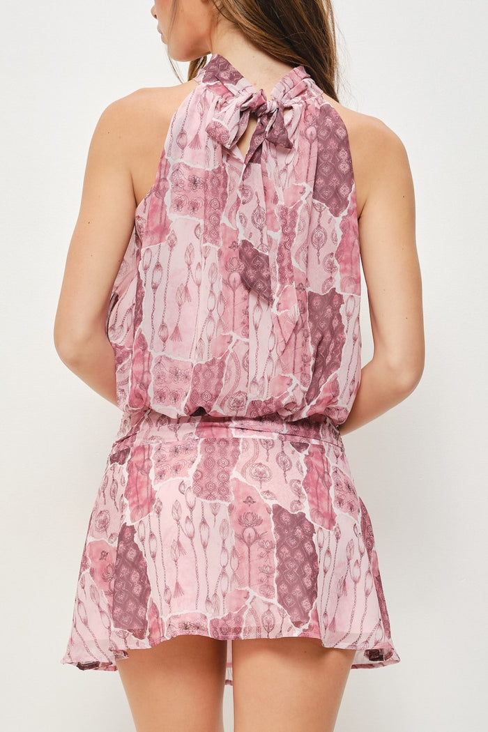 A woman shown from the back wearing a sleeveless halter-neck romper with a pink and mauve abstract print, photographed against a plain light background.