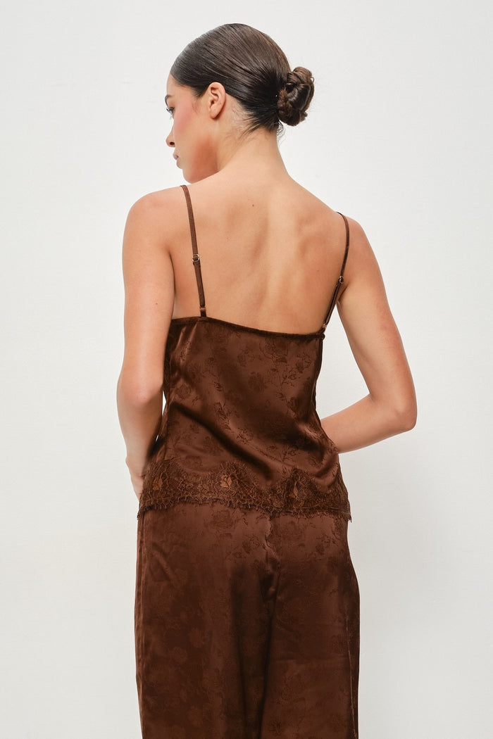 A woman shown from the back wearing a brown satin camisole top and matching wide-leg trousers against a plain light gray studio background.