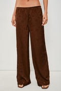 A person wearing loose, wide-leg brown pants with a drawstring waist and open-toe flat sandals, photographed against a plain light background.
