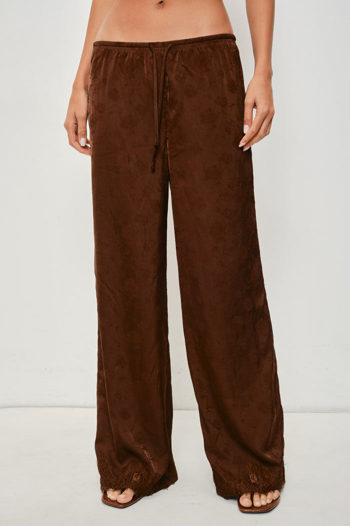 A person wearing loose, wide-leg brown pants with a drawstring waist and open-toe flat sandals, photographed against a plain light background.