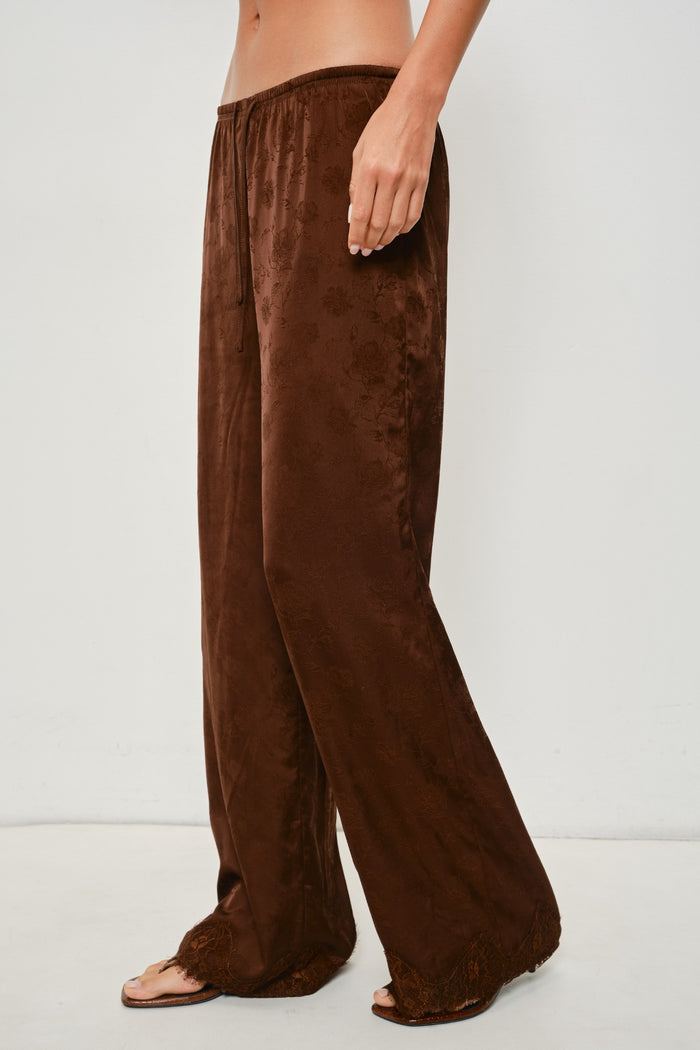A person wearing loose, wide-leg brown pants made of a soft textured fabric, shown from the waist down against a plain light background.