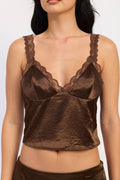 A close-up of a model wearing a brown satin camisole top with matching lace trim and a matching brown satin crop top.