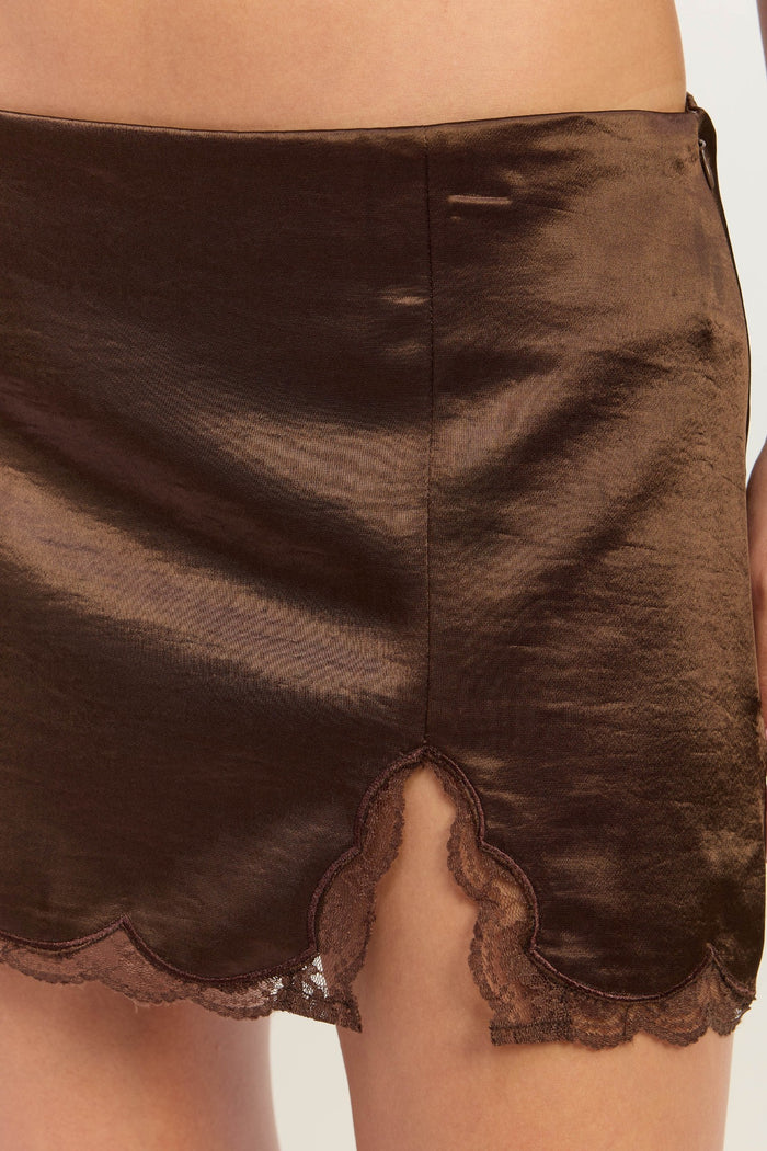 Close-up of a brown satin mini skirt with a scalloped lace hem, worn by a model.