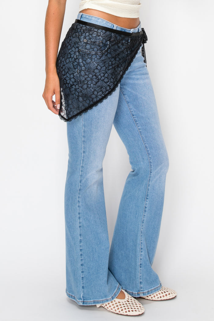 Woman wearing white top with denim pants and a black lace overlay against a plain background