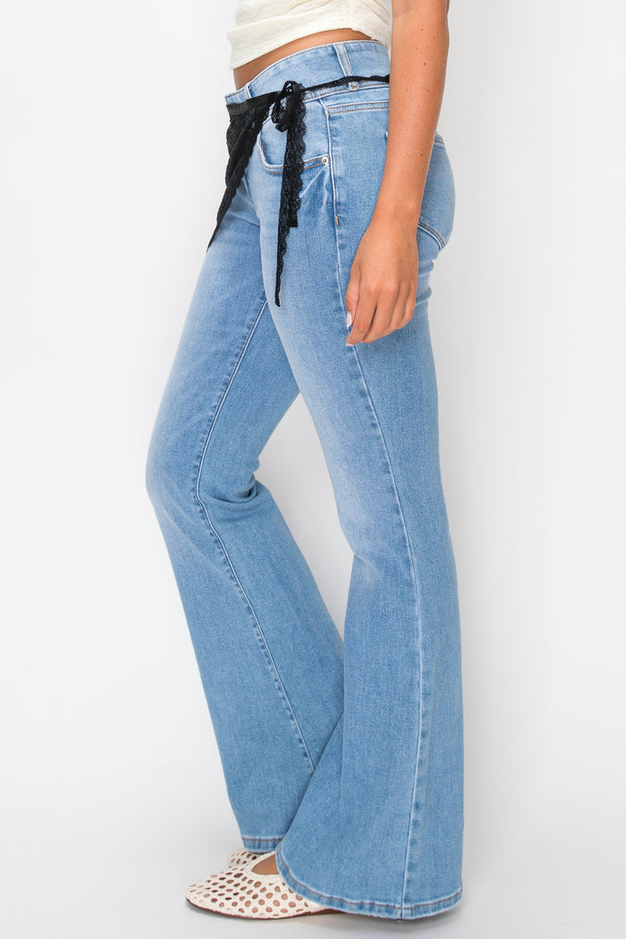 Woman wearing white top with denim pants and a black lace overlay against a plain background