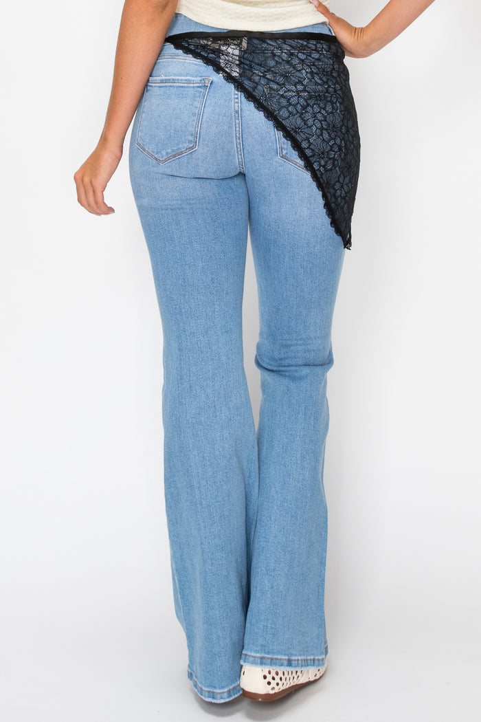 Woman wearing white top with denim pants and a black lace overlay against a plain background