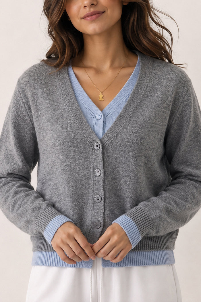A woman wearing a heather gray button-front cardigan with light blue ribbed trim over a light blue V-neck top, paired with white bottoms against a plain light background.