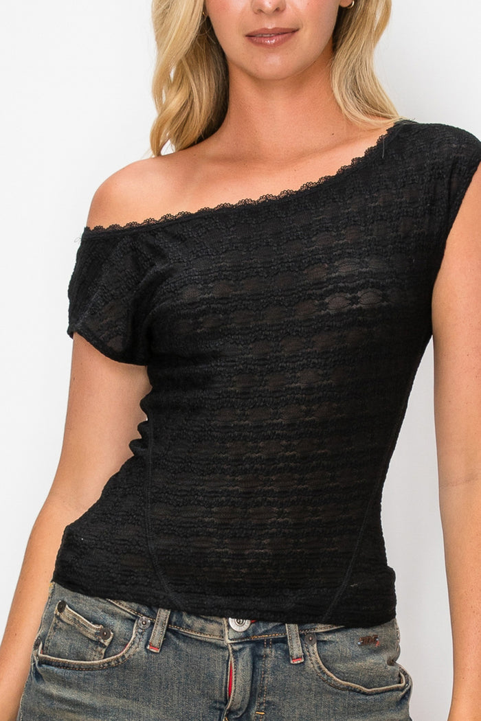 A woman wearing a black off-the-shoulder short-sleeve top with a textured, slub-like knit fabric and scalloped trim, paired with blue jeans.