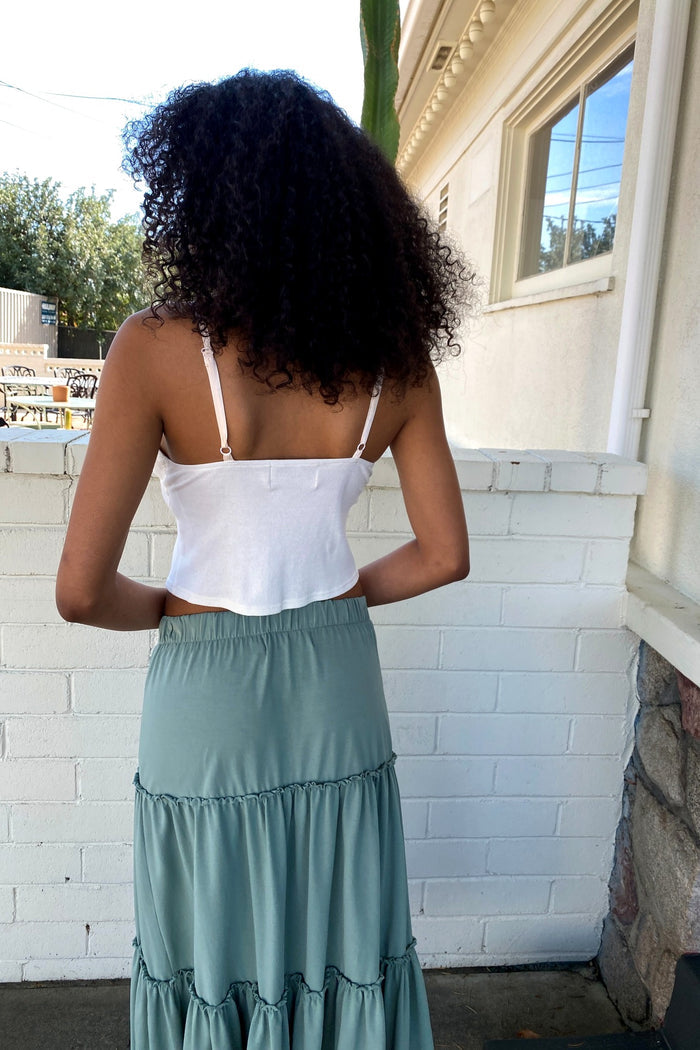 Woman wearing a white top and green skirt standing in front of a white brick wall.