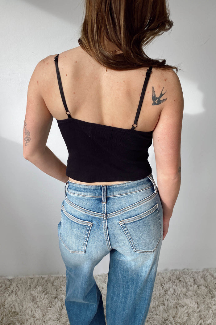 Person wearing a black top and blue jeans with a plain background