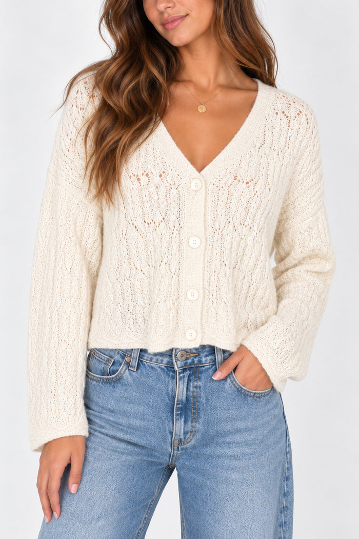 A woman wearing a cream cable-knit button-up cardigan sweater and light blue jeans, shown from the chest down against a plain light background.