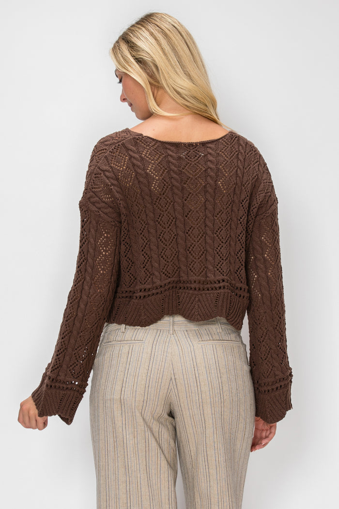 A woman shown from the back wearing a brown cable-knit cropped sweater and light beige pinstriped trousers against a light gray studio background.