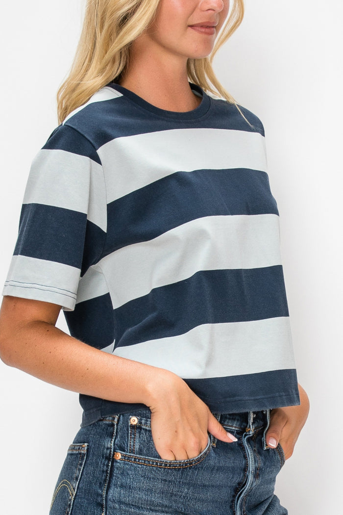 A woman wearing a cropped short-sleeve t-shirt with horizontal navy blue and light gray stripes, paired with blue jeans, shown from the side against a plain white background.