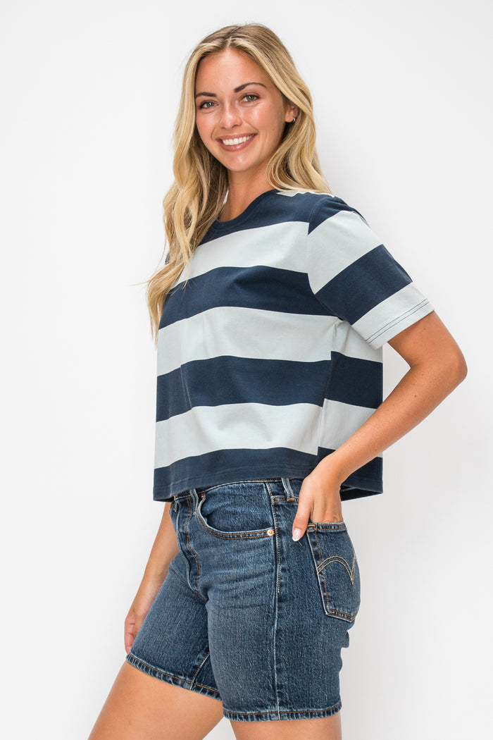 A woman modeling a short-sleeve striped t-shirt with navy blue and white horizontal stripes, paired with blue denim shorts, against a plain white background.