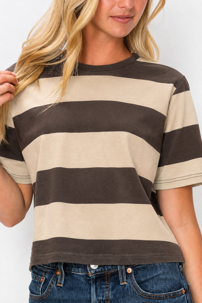 A woman wearing a cropped short-sleeve t-shirt with horizontal dark brown and beige stripes, paired with blue jeans, against a plain white background.