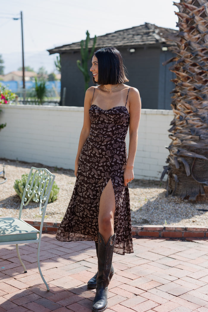 Woman in a floral dress and boots standing outdoors on a patio.